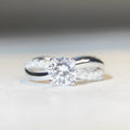 Silver geometric ring with a twisted band, a cross design, and a 1 karat moissanite in a four-claw setting.