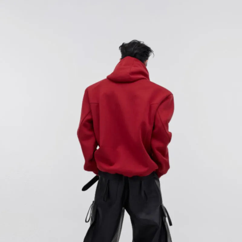 Man wearing a red loose-fit hooded sweater with a printed metal graphic design on the front.
