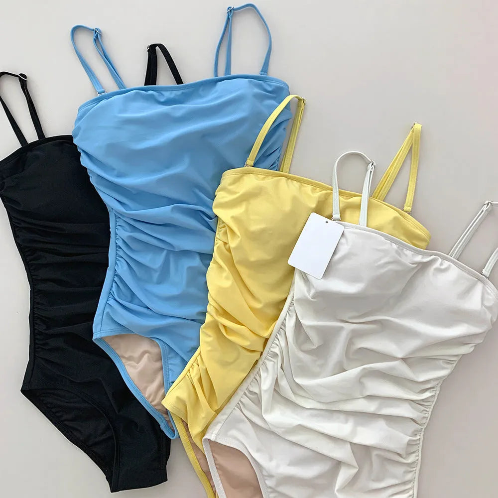 Sling style one-piece swimsuit with belly pleats in slim fit, available in black, blue, white, and yellow.