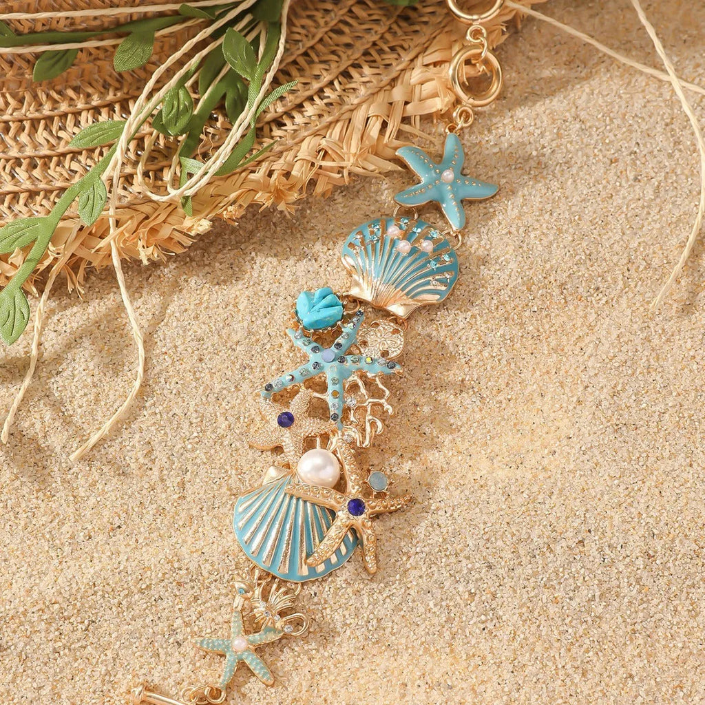 Turquoise alloy bracelet with a rhinestone boat anchor and starfish charm on a model's wrist.