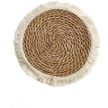Round natural papyrus straw placemat with tassel detailing on a table.