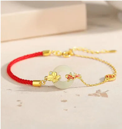 Gold and red women's bracelet with a silver peace buckle, red rope, and Hetian jade charm.