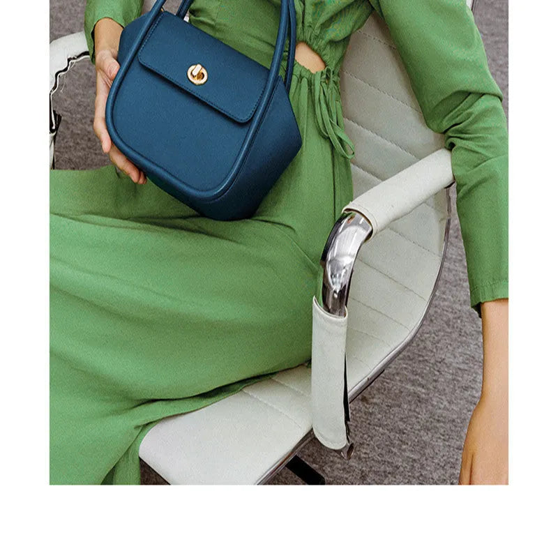 Women's winged leather handbag with cross-body strap in blue, showing latch closure and buckle detail.