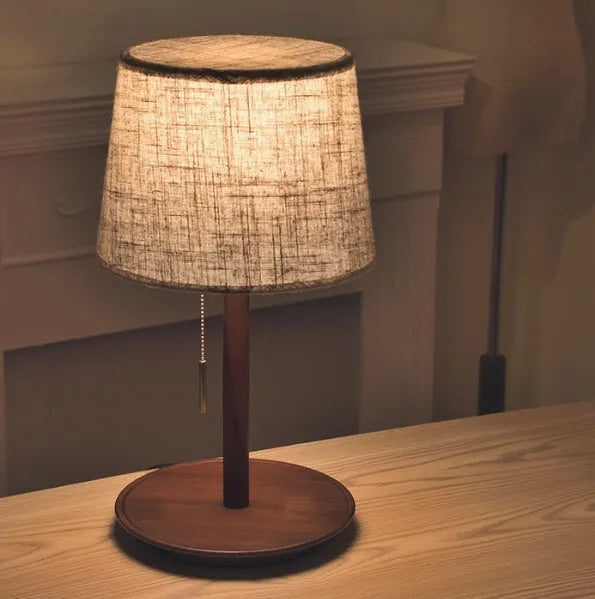 Walnut coloured solid wood desk lamp with a white cloth lampshade and a black cable switch.
