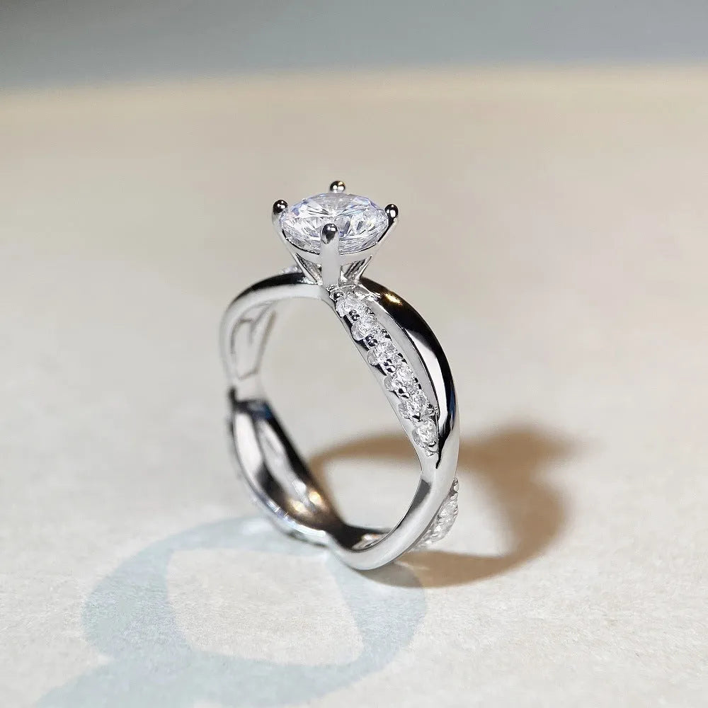 Silver geometric ring with a twisted band, a cross design, and a 1 karat moissanite in a four-claw setting.