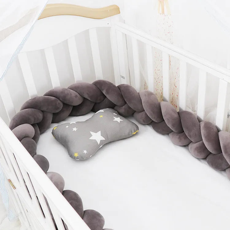 Braided knot design crib bumper in spandex velvet, shown in a light grey colour wrapped around crib slats.