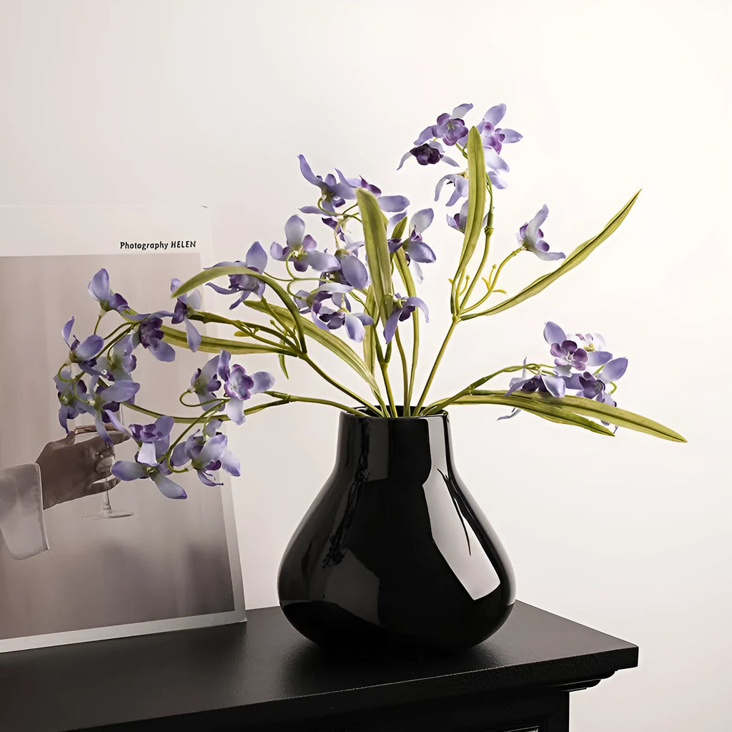 Black ceramic modern vase with white artificial orchid stems on wooden table