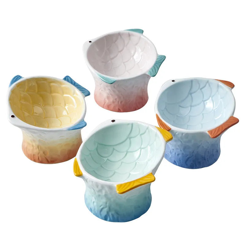 Four coloured fish-shaped ceramic pet bowls with a tilted, elevated design on a plain surface.