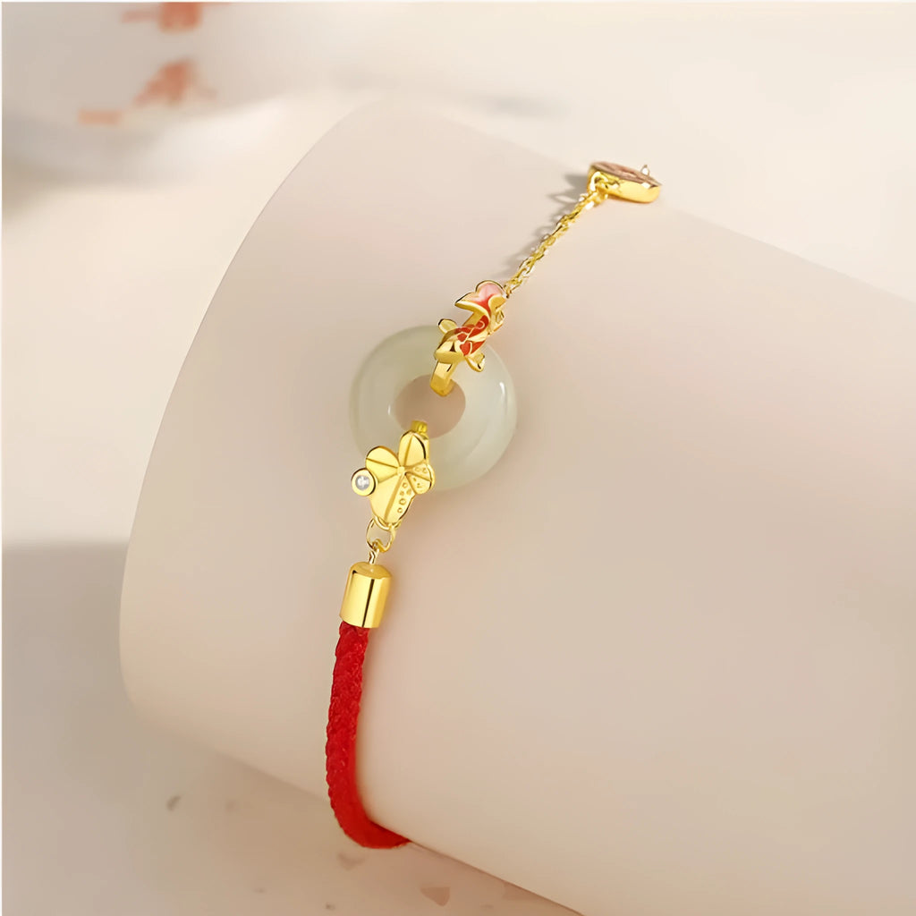 Gold and red women's bracelet with a silver peace buckle, red rope, and Hetian jade charm.