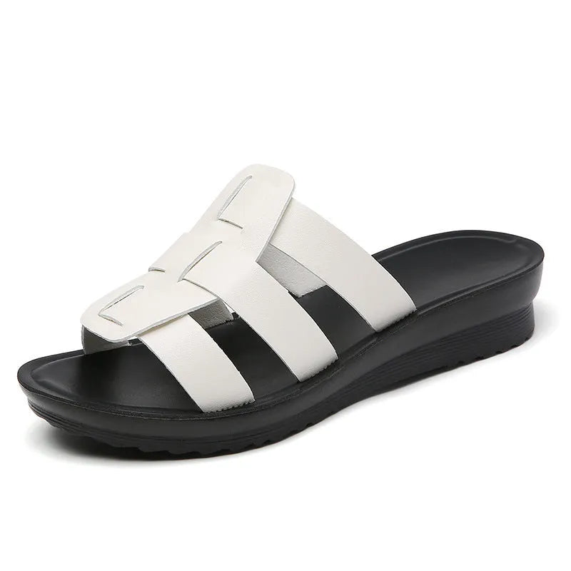 Beige women's flat-bottom slippers with waxed leather upper and soft PU sole on a wooden floor.