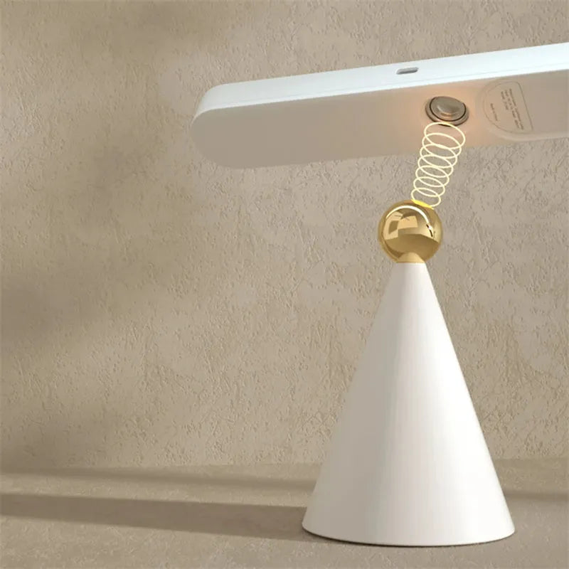 Geometric shaped white desk lamp with a magnetic base on a wooden table next to a book.