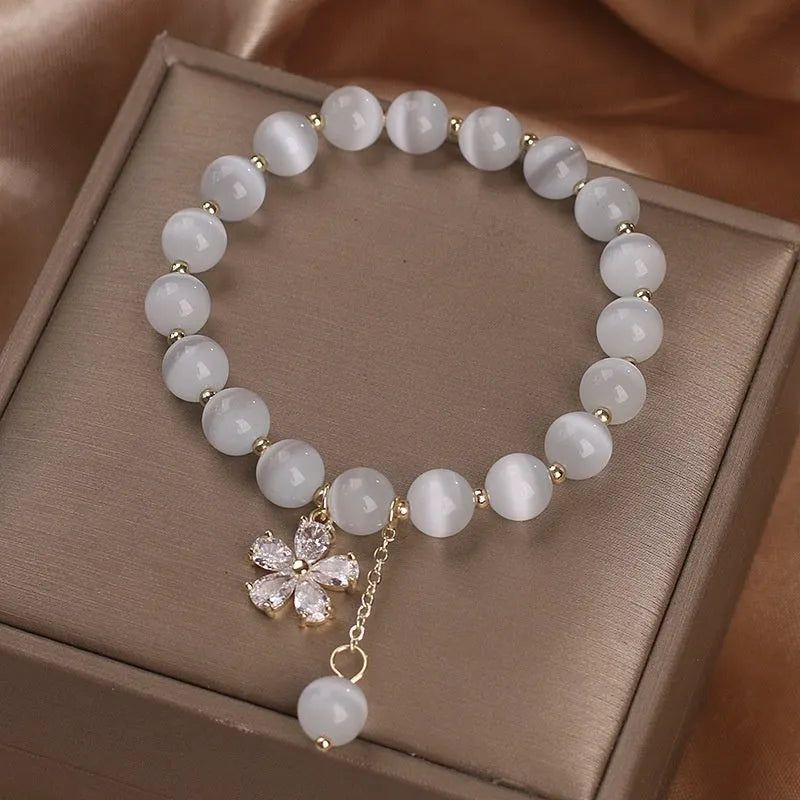Women's single loop white cat's eye crystal bracelet with flower pattern and tassels, showing safety buckle clasp