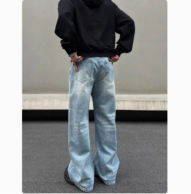 Man wearing blue straight leg jeans with whisker wash detailing and a flared leg style.