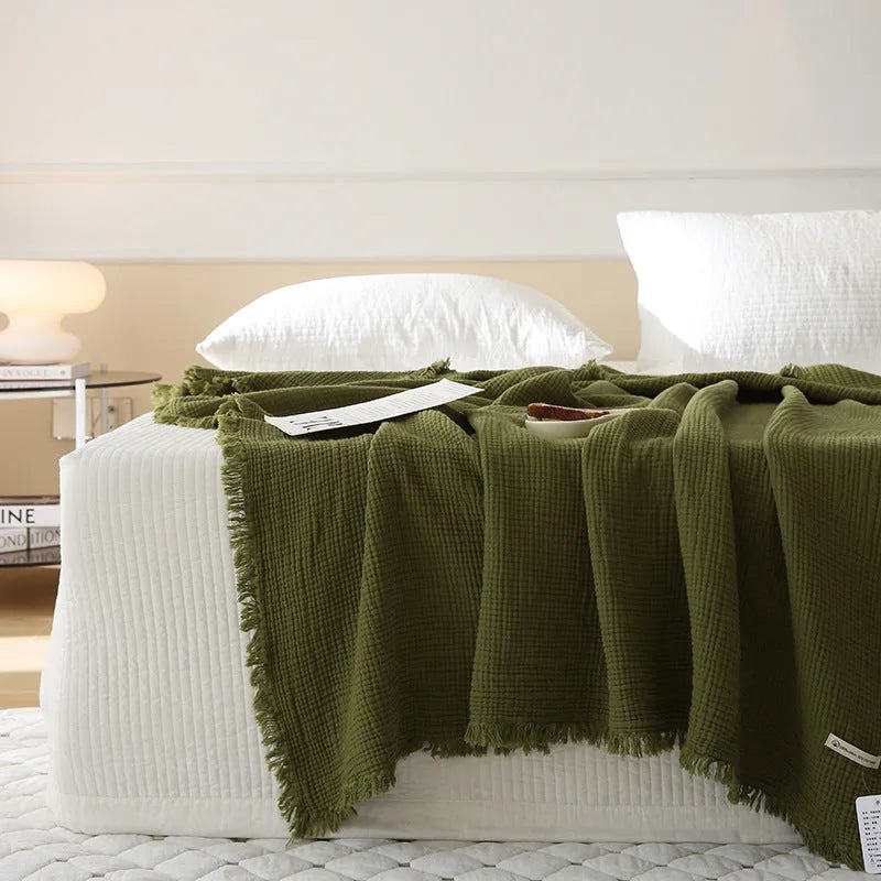 Cotton four-layer gauze blanket with tassel trim in avocado green colour on a chair.
