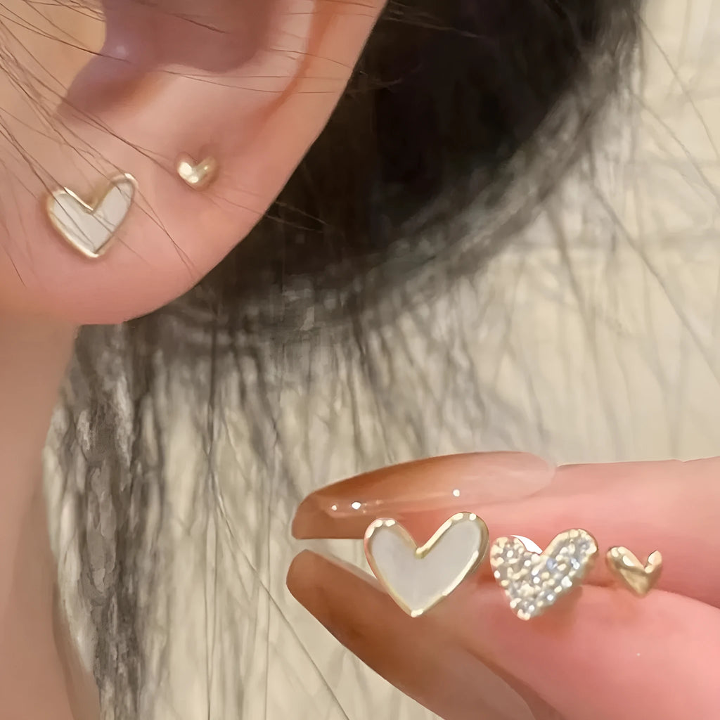 Set of three pairs of women's heart-shaped alloy earrings in gold, black, pink, and black-white colours.