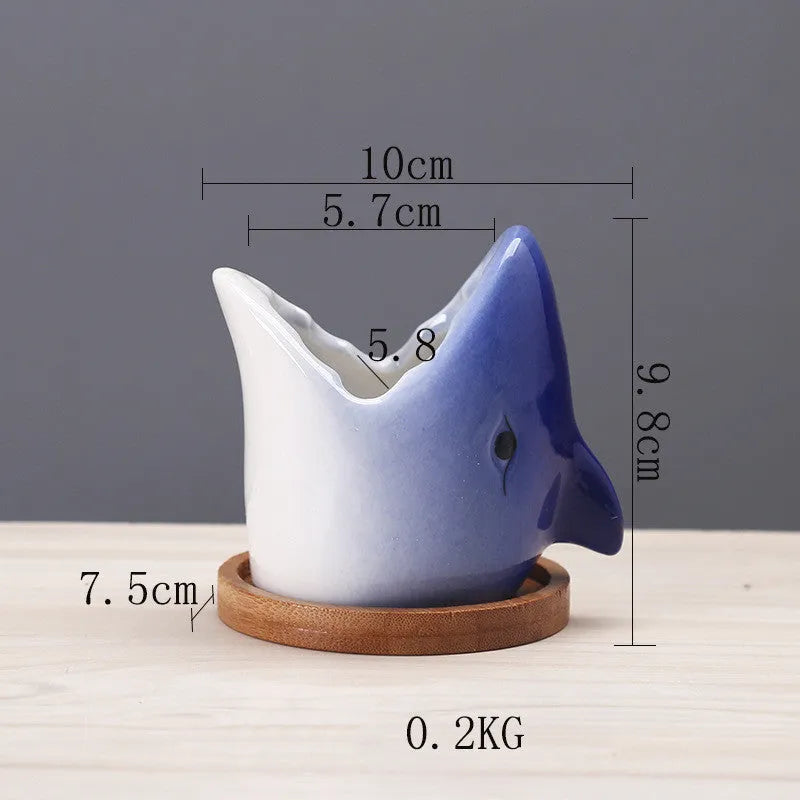 Cartoon ceramic succulent pot with drainage hole in blue on a desktop with small plants