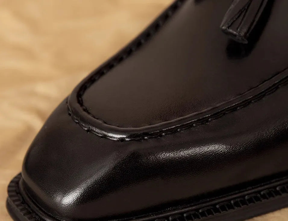 Men's black genuine leather slip-on loafers with fringe detail and rubber sole.