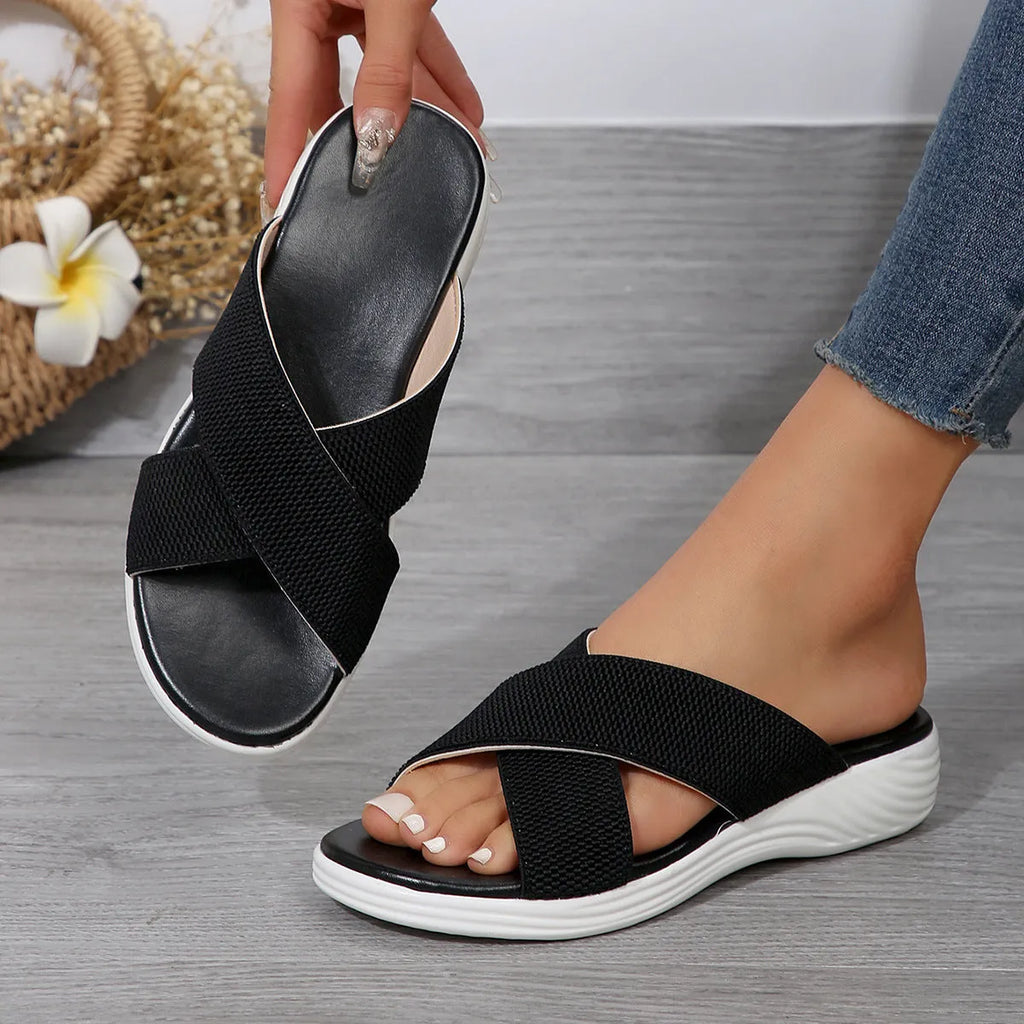 Black wedge slippers with peep toe and thick rubber sole on a grey background.