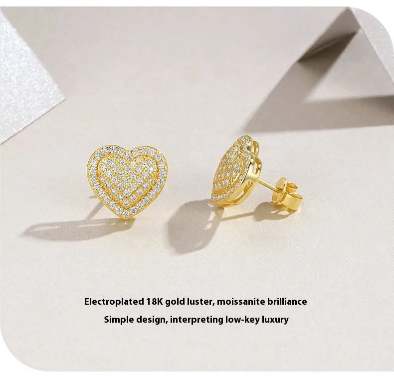 A pair of simple gold-tone heart-shaped stud earrings with a moissanite stone, shown from the front.