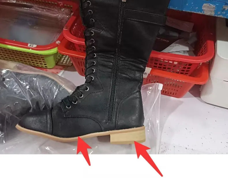 Black women's knee high boots with cross strap and lace-up front design on a white background.