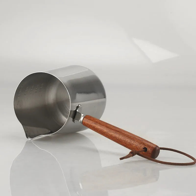Stainless steel milk frothing pitcher with interior measurement scale and wooden handle
