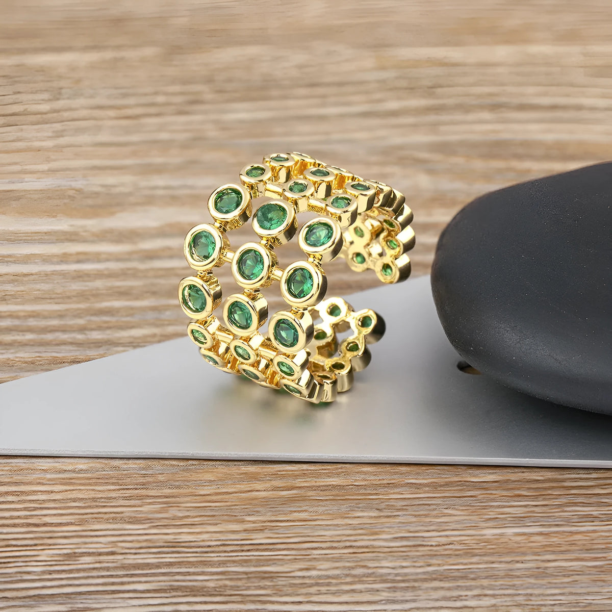 Close-up of a wide, layered copper ring with 18K gold plating and green zircon stones.