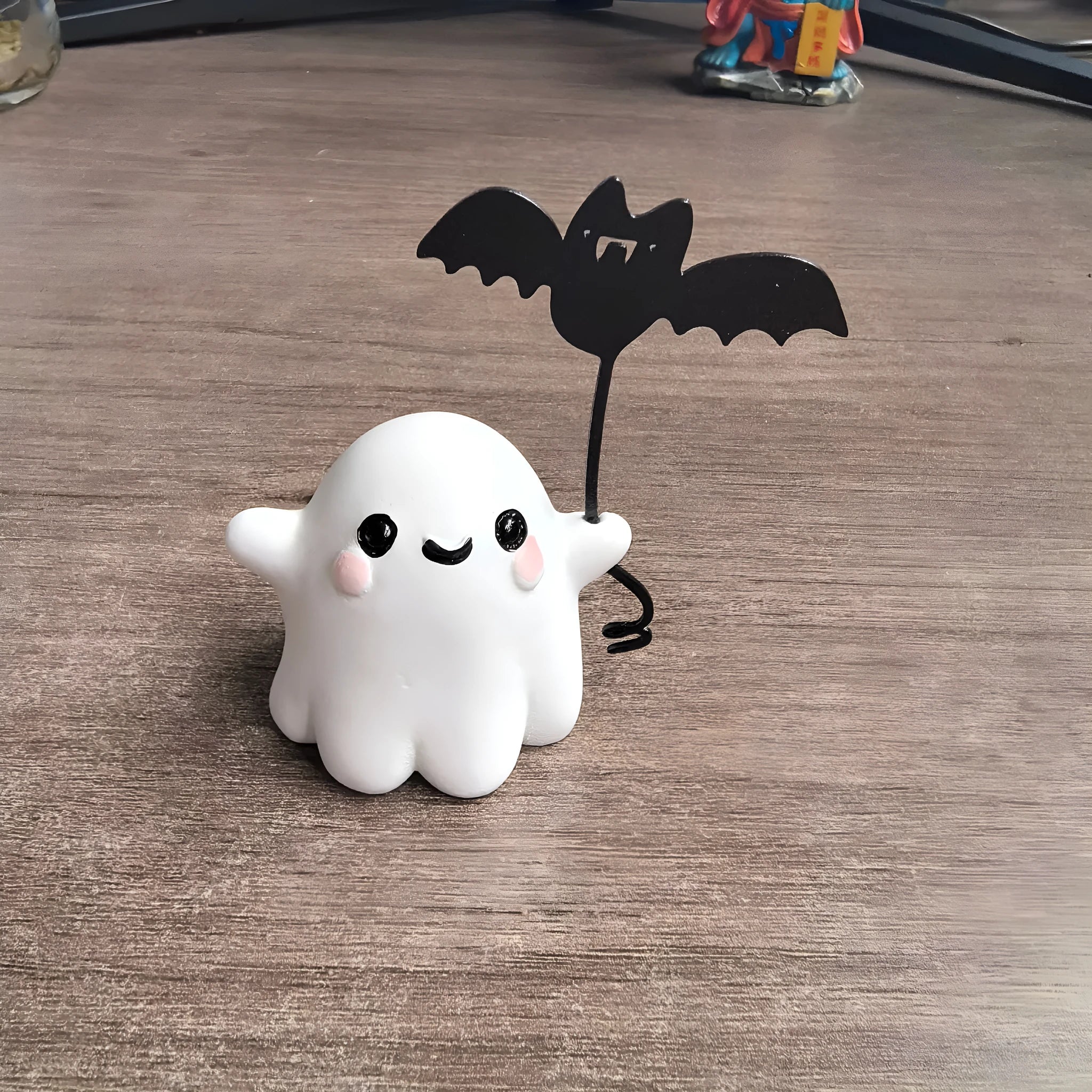 Miniature resin ghost figurine holding a bat, a compact Halloween decoration ornament.