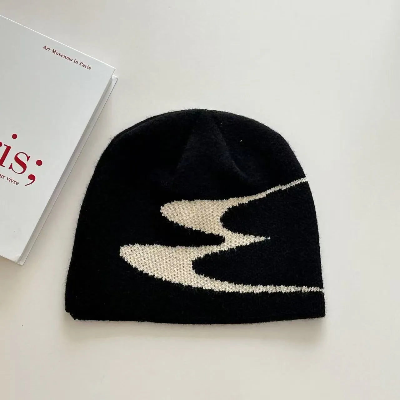 Acrylic knit beanie hat in black on a grey background, showing ribbed texture.
