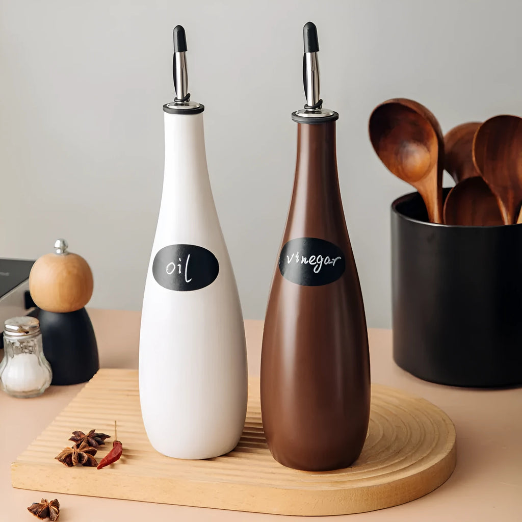Black conical ceramic oil pot with funnel top and oil brush on a kitchen counter.
