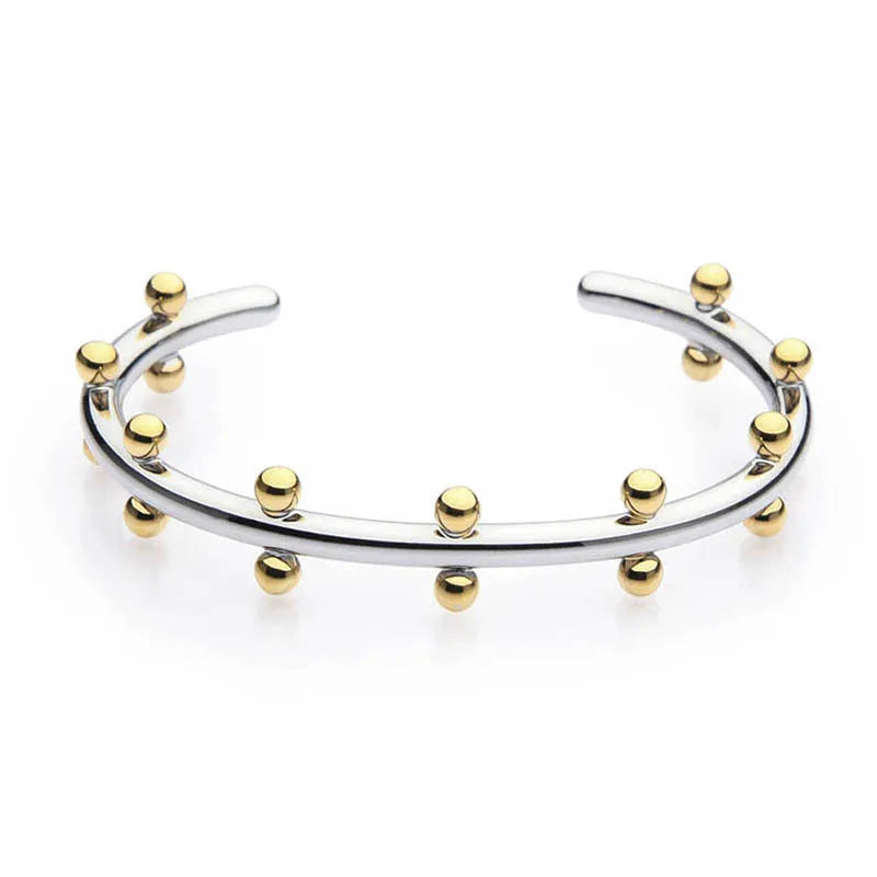 Close-up of a C-shaped stainless steel bean bead with textured rivet design, next to an alloy bracelet.