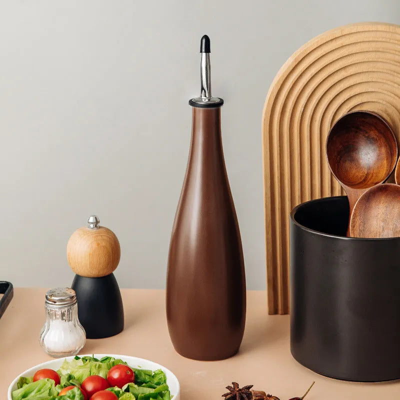 Black conical ceramic oil pot with funnel top and oil brush on a kitchen counter.