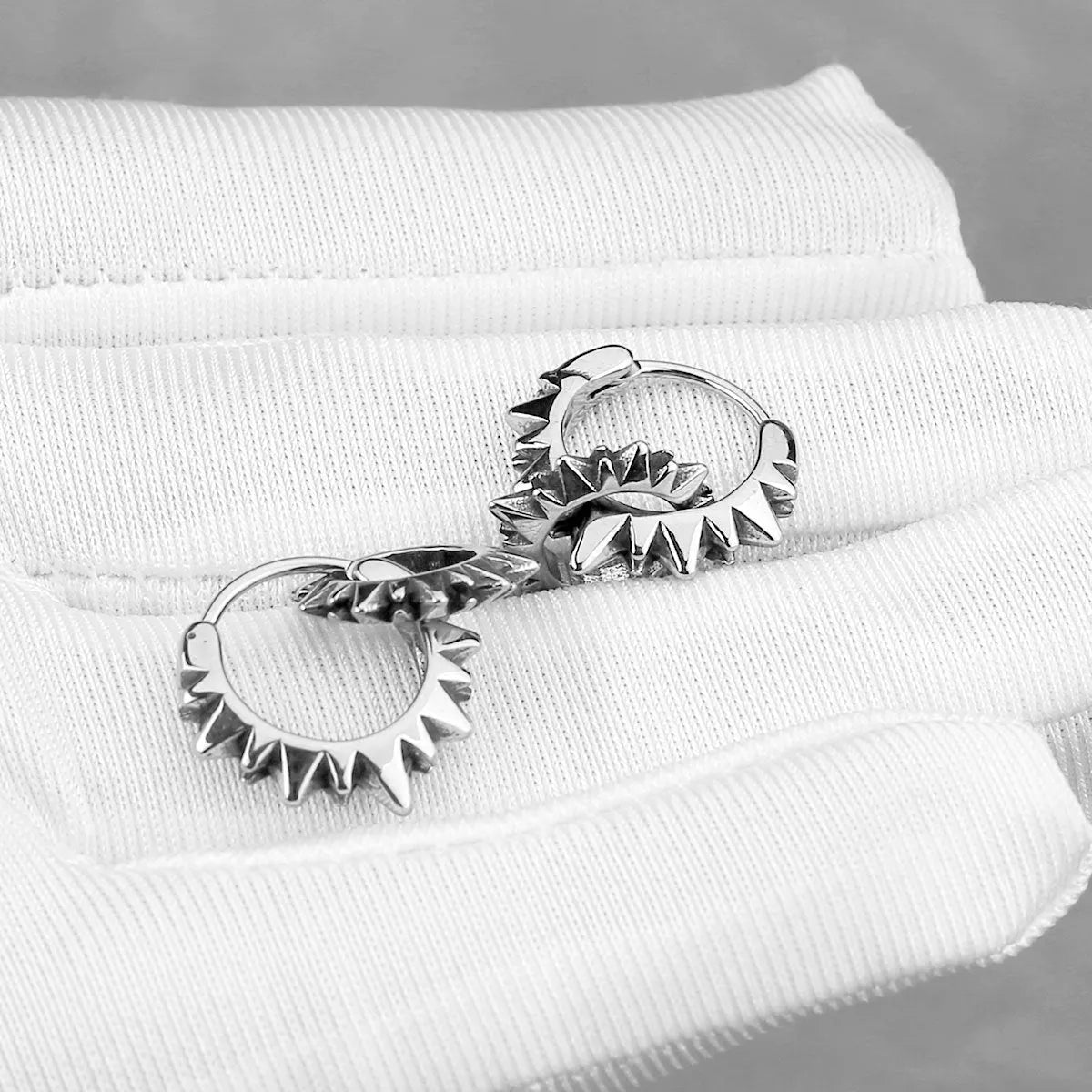 A pair of polished stainless steel round ring earrings with a steel colour finish on a white background.