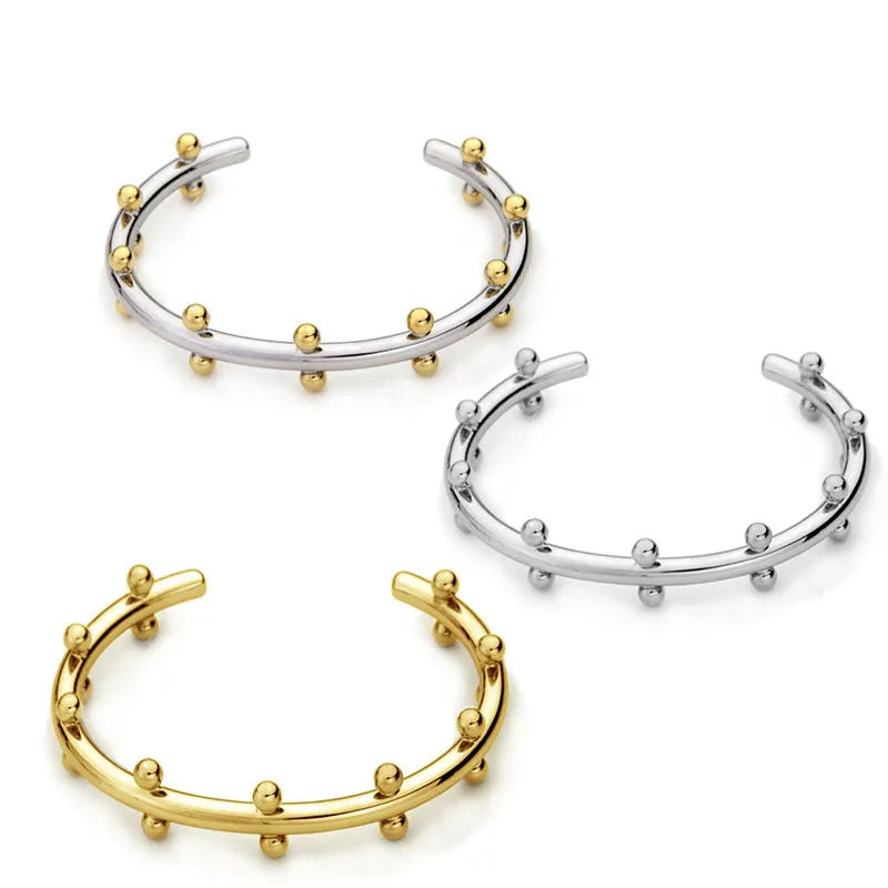 Close-up of a C-shaped stainless steel bean bead with textured rivet design, next to an alloy bracelet.