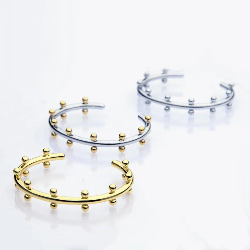 Close-up of a C-shaped stainless steel bean bead with textured rivet design, next to an alloy bracelet.