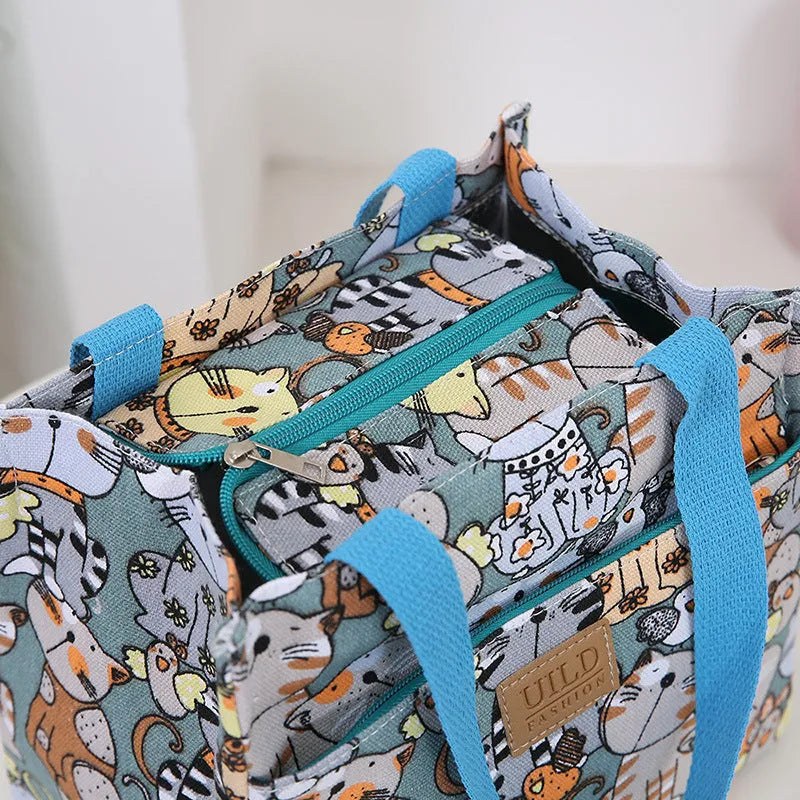 Women's printed canvas handbag showing floral or cat design on black, blue or pink background