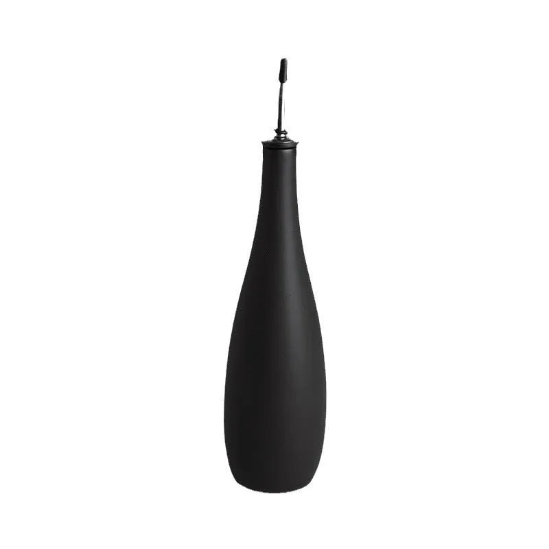 Black conical ceramic oil pot with funnel top and oil brush on a kitchen counter.