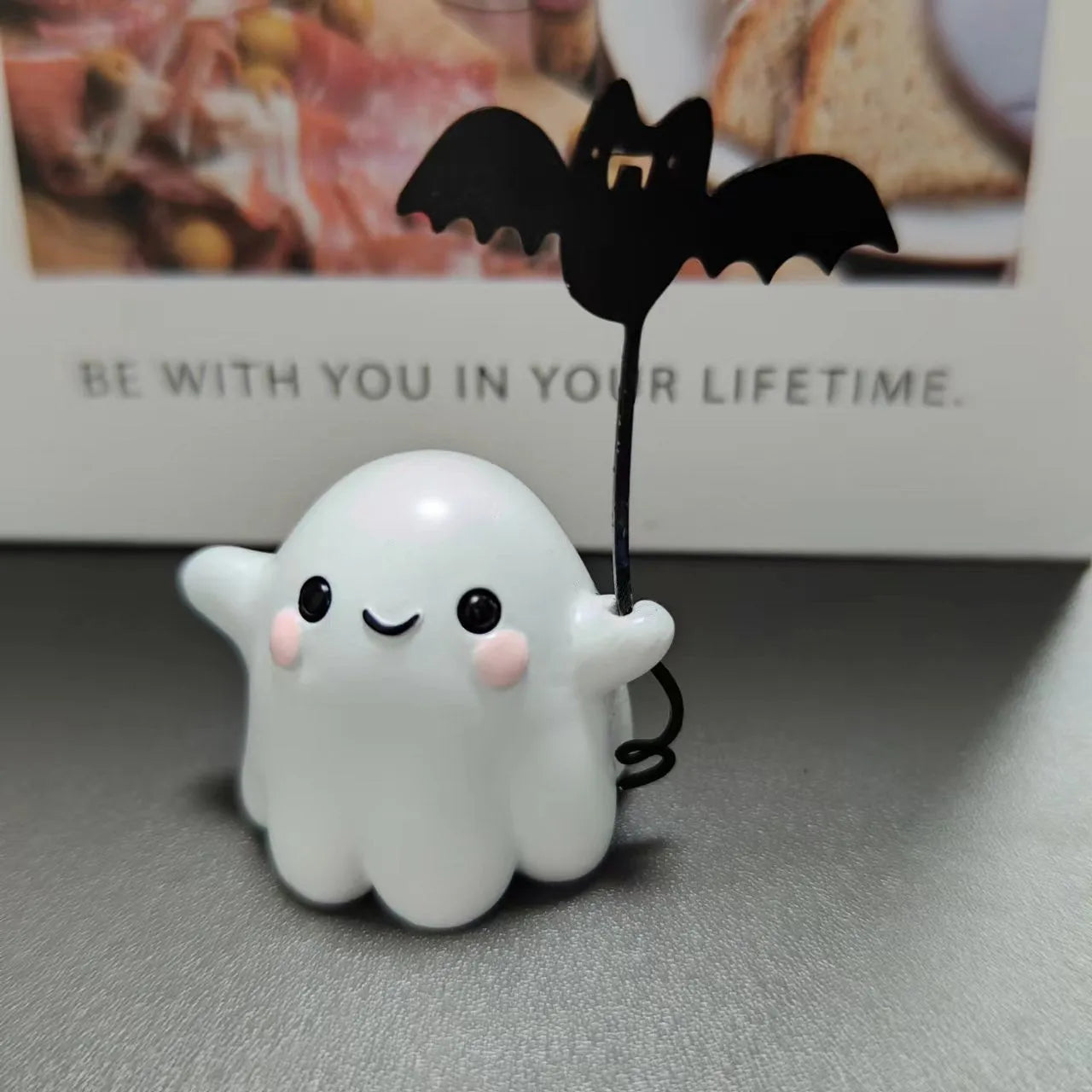 Miniature resin ghost figurine holding a bat, a compact Halloween decoration ornament.