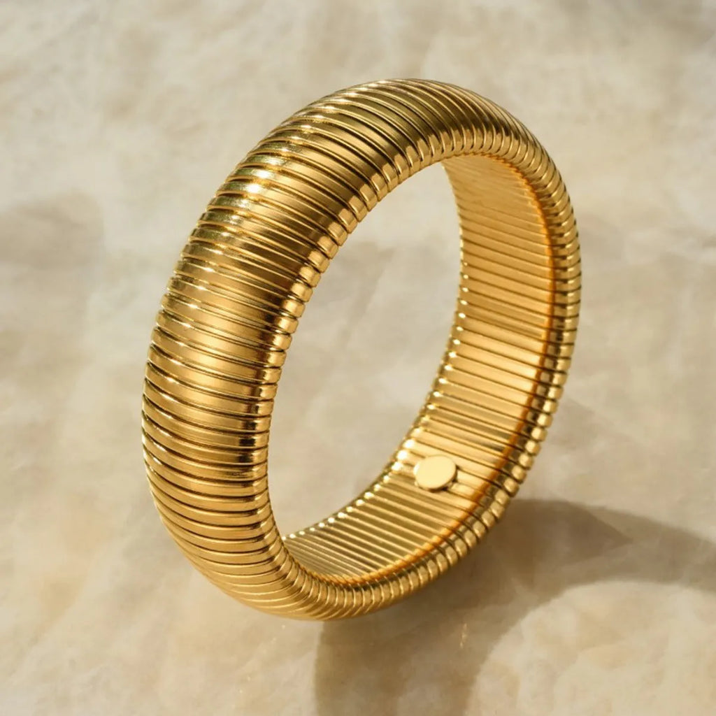 Close-up of a women's titanium steel bracelet with an exaggerated vertical stripe ring elastic design in a gold finish.