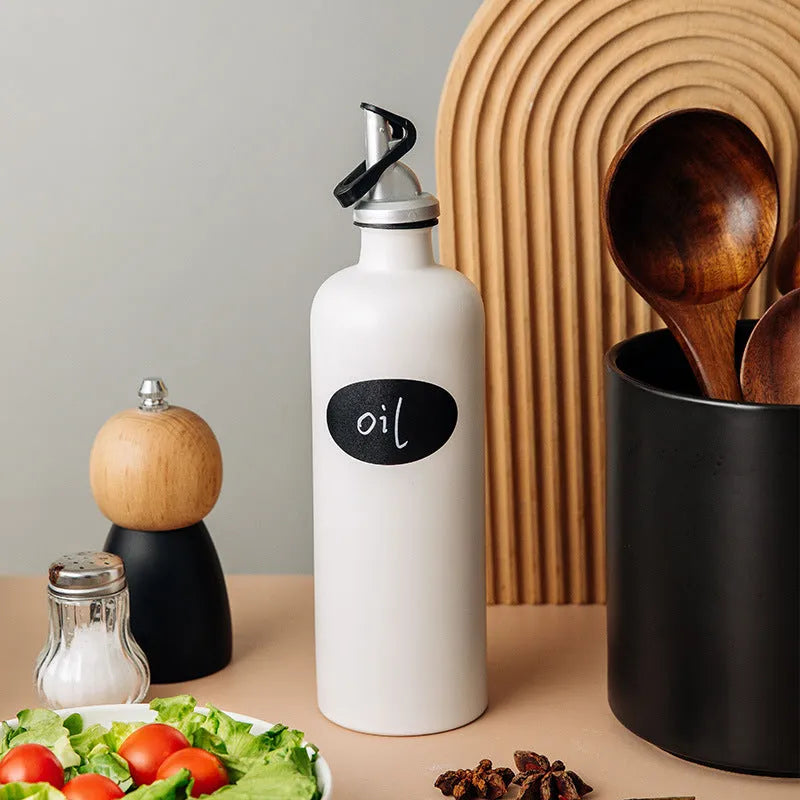 Black conical ceramic oil pot with funnel top and oil brush on a kitchen counter.
