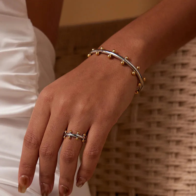 Close-up of a C-shaped stainless steel bean bead with textured rivet design, next to an alloy bracelet.