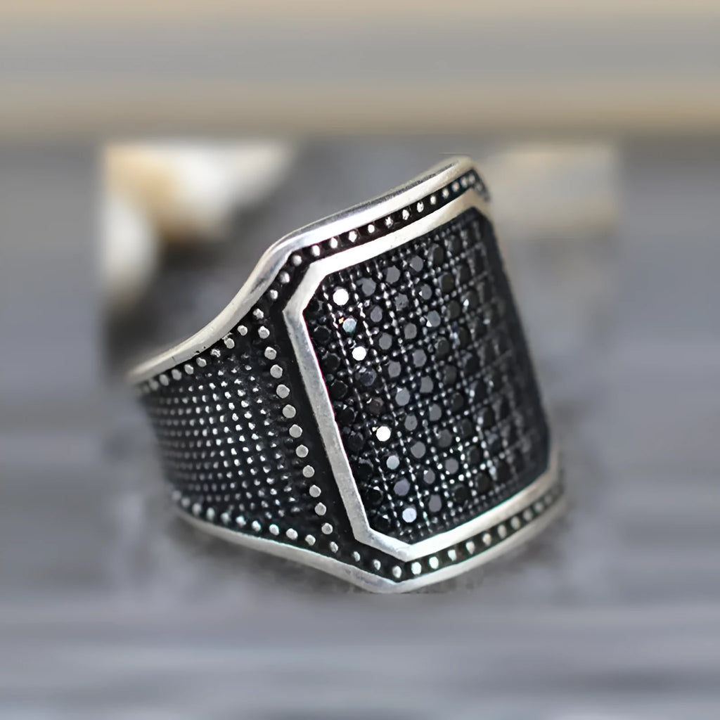 Black alloy ring with copper inlay detail and set zircon stones on a hand.
