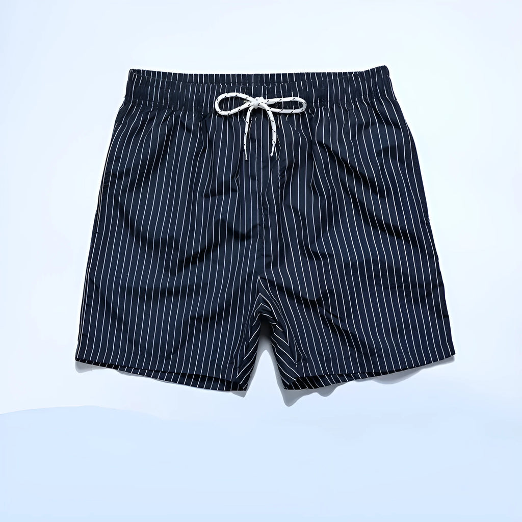 A man wearing grey striped polyester beach shorts with a straight leg opening, shown on a beach.