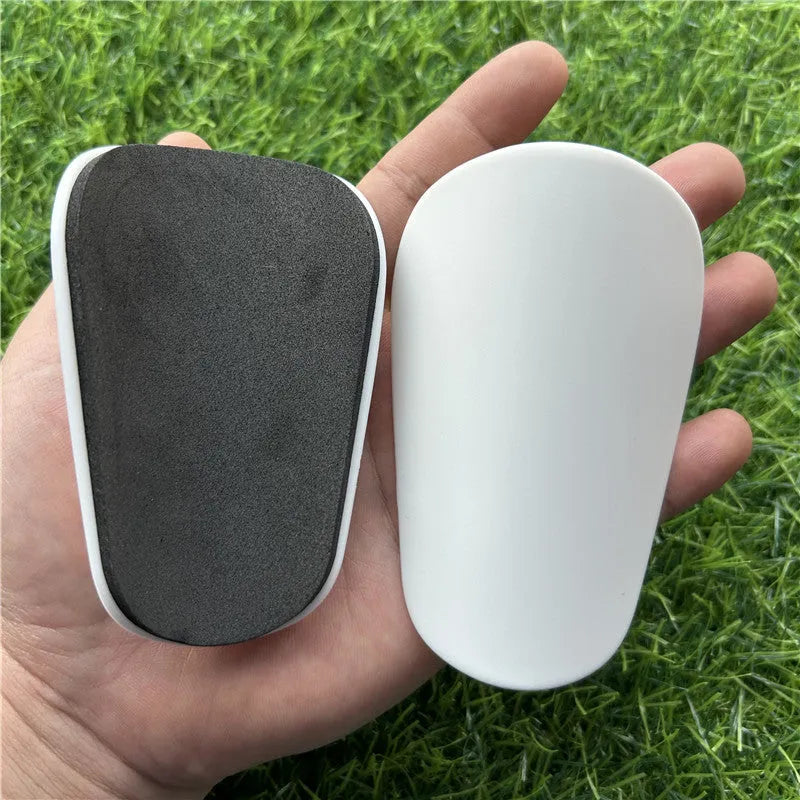 Extra small mini plastic football shin guards for kids in black and white, measuring 8 by 5 centimetres.