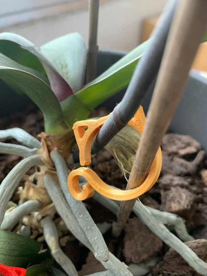 Small red plastic cat-shaped clip for holding plant stems, shown next to a leaf for scale.