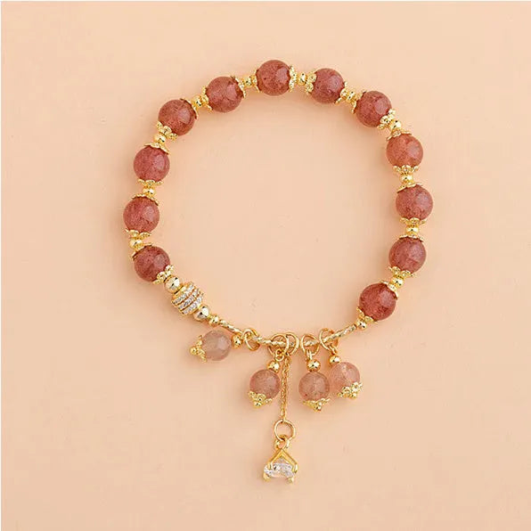 Close-up of a women's pink crystal bracelet with a heart-shaped Strawberry Quartz stone and a white pearl accent.
