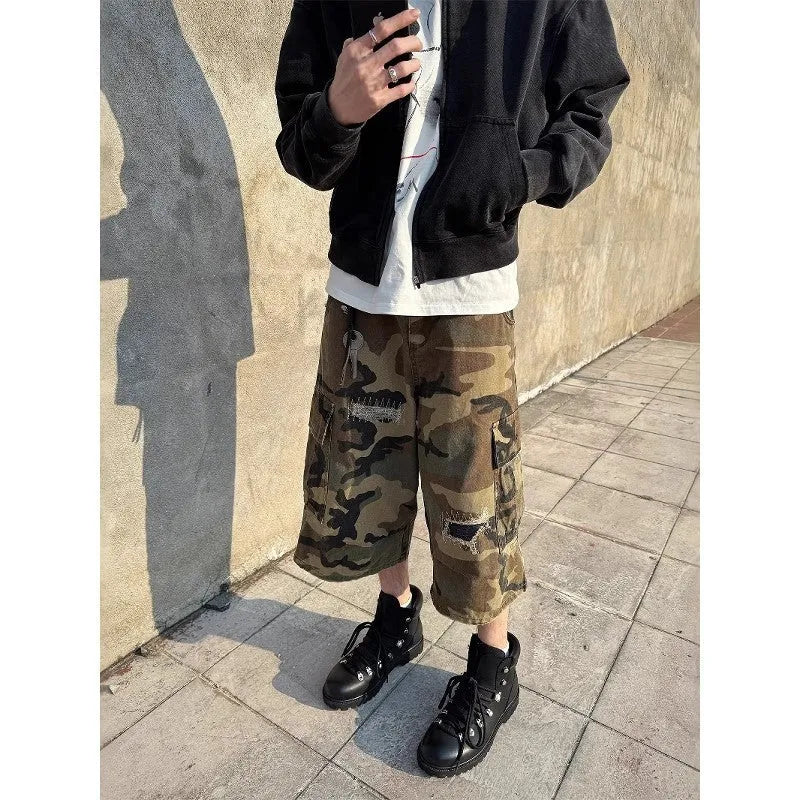 Man wearing loose fit camouflage print cropped jeans with ripped knees and patchwork details.