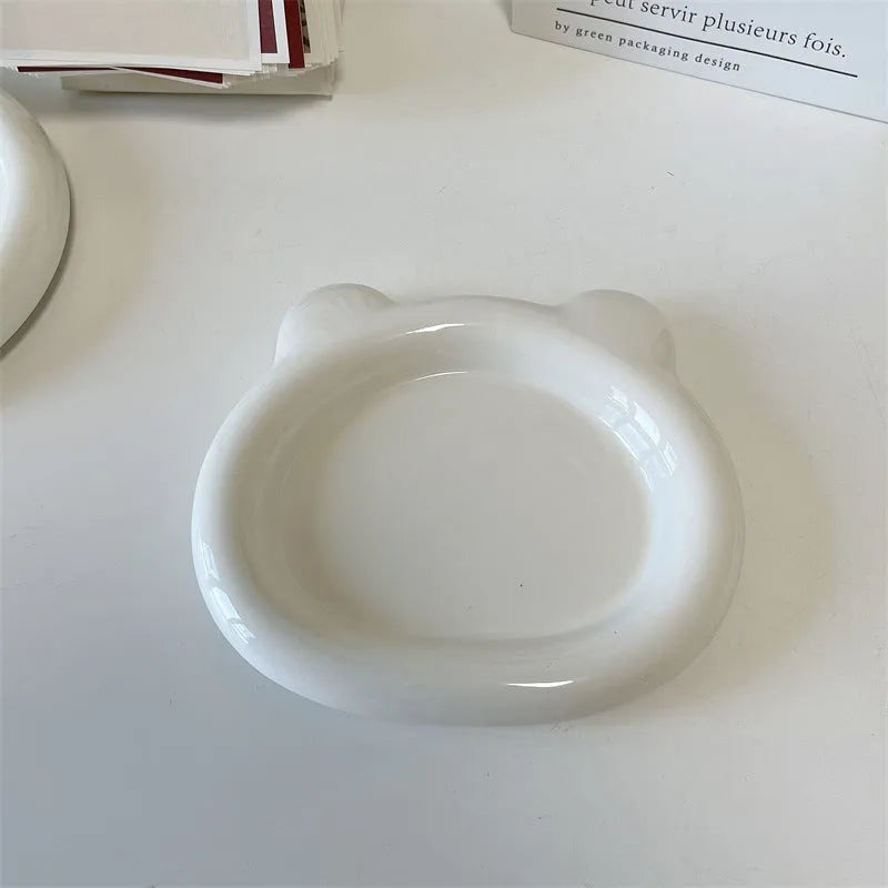 White porcelain plant saucer with a bear doodle design, shown next to a potted plant.