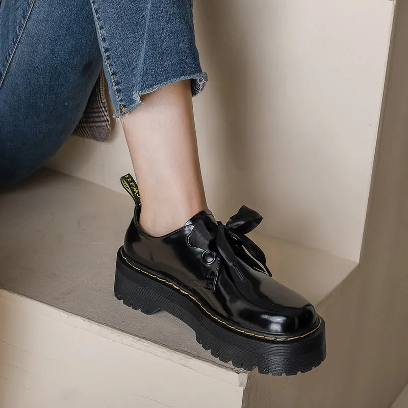 Black thick soled women's lace-up shoes with ribbon and cross strap details on a white background.