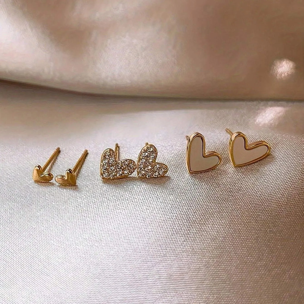 Set of three pairs of women's heart-shaped alloy earrings in gold, black, pink, and black-white colours.