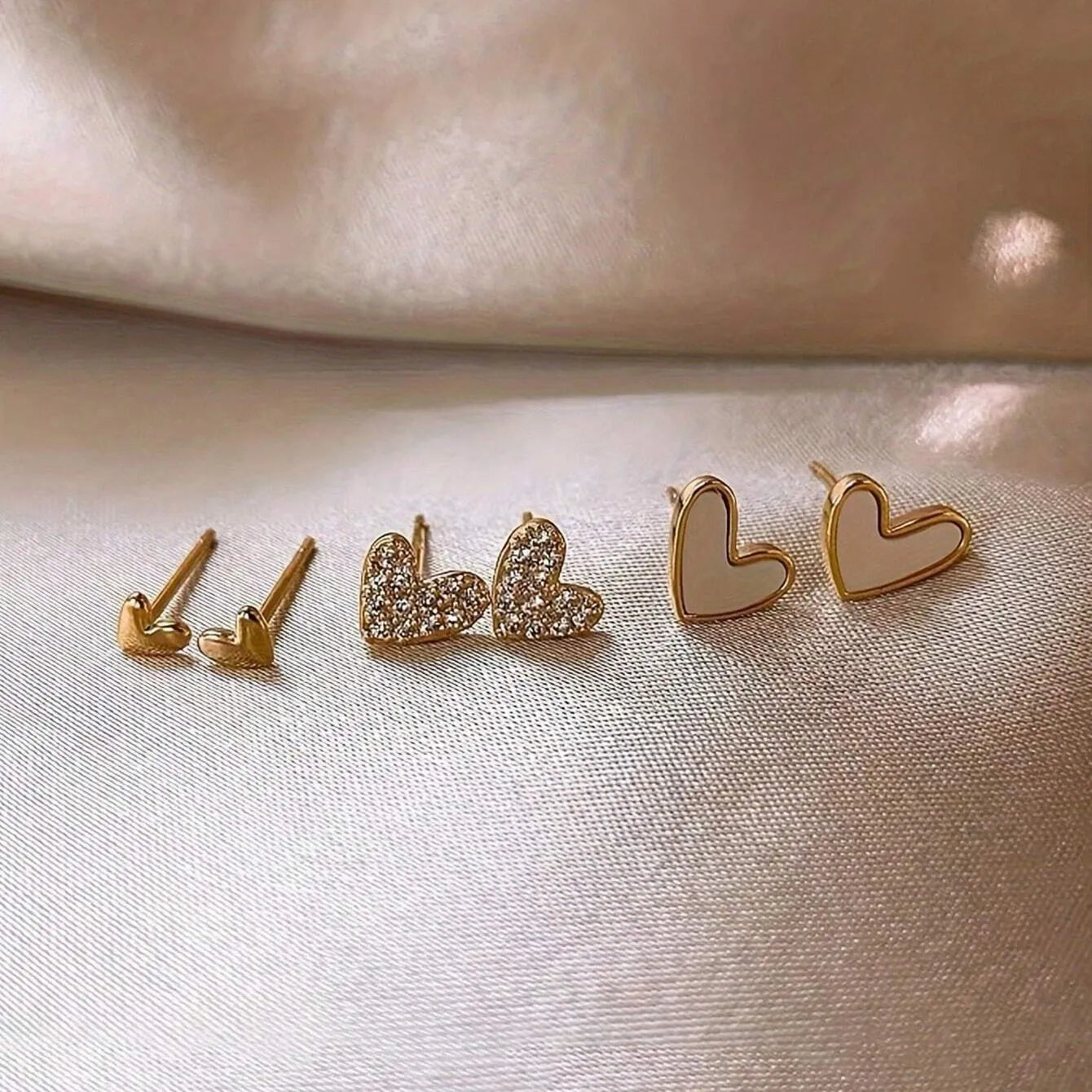 Set of three pairs of women's heart-shaped alloy earrings in gold, black, pink, and black-white colours.